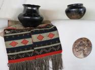 Hopi sash, ca. 1880–1890, 18.5 x 47 in. Two-piece handwoven embroidered sash sewn together with red yarn. White woven cotton fabric with weave of red, green, black, and white yarn wefts on white cotton warp. One panel longer, fringe. On a fireplace mantel in the Couse Home with northern New Mexico Pueblo pottery and a ceramic insert attributed to Nampeyo (Hopi). E. I. Couse Collection.