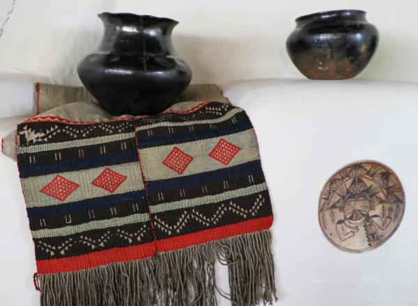 Hopi sash, ca. 1880–1890, 18.5 x 47 in. Two-piece handwoven embroidered sash sewn together with red yarn. White woven cotton fabric with weave of red, green, black, and white yarn wefts on white cotton warp. One panel longer, fringe. On a fireplace mantel in the Couse Home with northern New Mexico Pueblo pottery and a ceramic insert attributed to Nampeyo (Hopi). E. I. Couse Collection.